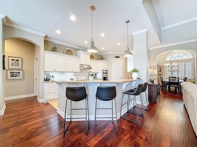 13248 Linzia Ln, Spring Hill, FL 34609 - kitchen featuring arched walkways, a kitchen breakfast bar, dark wood-type flooring, white cabinets, and tasteful backsplash