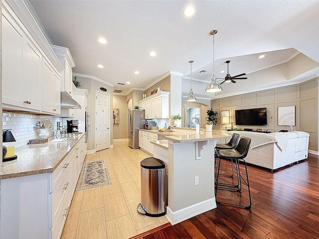 13248 Linzia Ln, Spring Hill, FL 34609 - kitchen featuring ceiling fan, ornamental molding, freestanding refrigerator, under cabinet range hood, and a kitchen bar