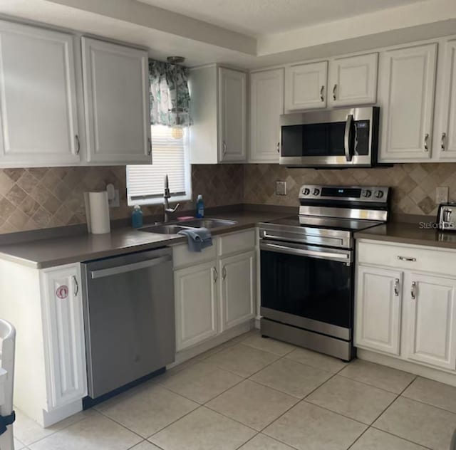 6603 Adams St, New Port Richey, FL 34652 - kitchen featuring appliances with stainless steel finishes, a sink, dark countertops, light tile patterned flooring, and white cabinets