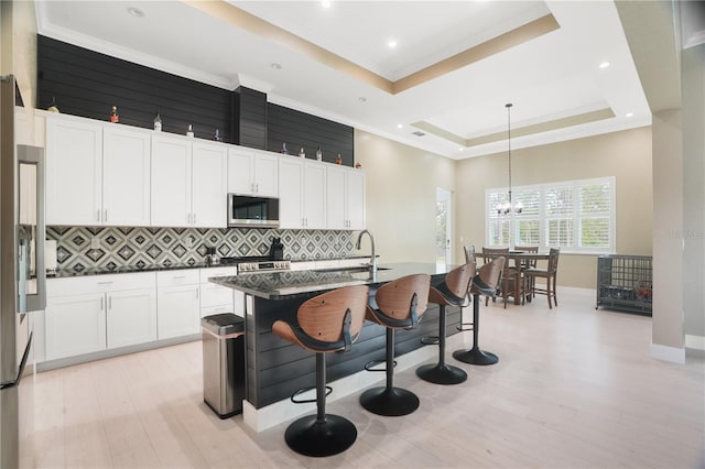 10380 Yellow Hammer Rd, Weeki Wachee, FL 34614 - kitchen with stainless steel appliances, a tray ceiling, tasteful backsplash, a kitchen bar, and light wood finished floors
