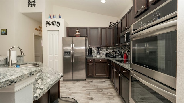 12458 Fish Cove Dr, Spring Hill, FL 34609 - kitchen featuring appliances with stainless steel finishes, a sink, lofted ceiling, dark brown cabinetry, and backsplash