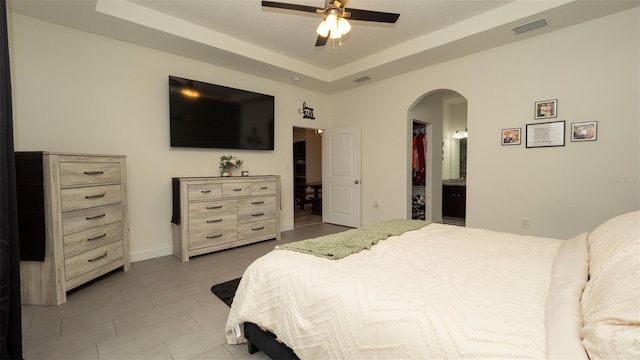 12458 Fish Cove Dr, Spring Hill, FL 34609 - bedroom featuring arched walkways, light tile patterned flooring, ensuite bath, a tray ceiling, and a ceiling fan