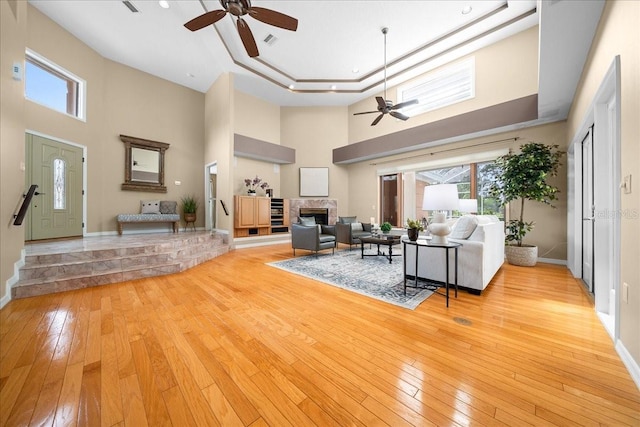 10044 Twelve Oaks Ct, Weeki Wachee, FL 34613 - living area with a ceiling fan, a high ceiling, a fireplace, light wood-style floors, and baseboards