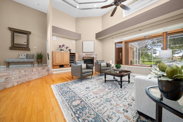 10044 Twelve Oaks Ct, Weeki Wachee, FL 34613 - living area featuring a towering ceiling, light wood finished floors, ceiling fan, a premium fireplace, and baseboards