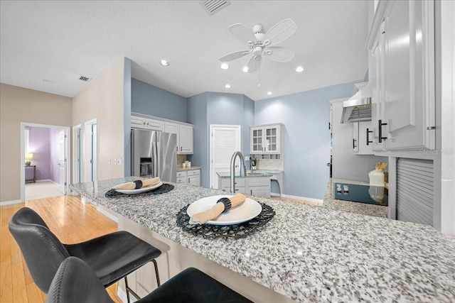10044 Twelve Oaks Ct, Weeki Wachee, FL 34613 - kitchen featuring stainless steel fridge, a peninsula, ceiling fan, white cabinets, and a breakfast bar