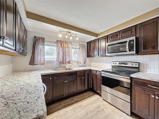 7119 Lenape Cir, New Port Richey, FL 34653 - kitchen featuring appliances with stainless steel finishes, a sink, light wood-style floors, dark brown cabinets, and light stone countertops