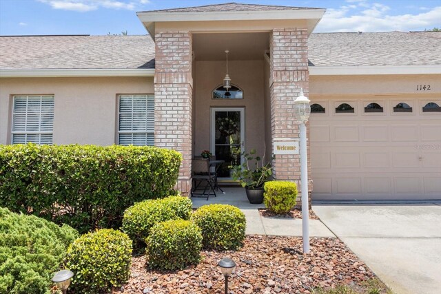 1142 Wolford Dr, Trinity, FL 34655 - view of exterior entry with brick siding, roof with shingles, stucco siding, a garage, and driveway
