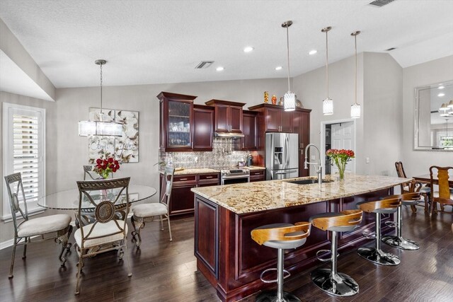 1142 Wolford Dr, Trinity, FL 34655 - kitchen with stainless steel appliances, vaulted ceiling, reddish brown cabinets, a sink, and dark wood-style floors
