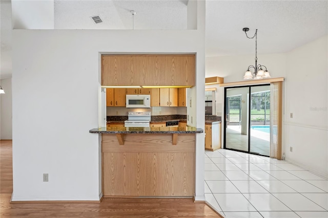 128 Oak Lake Dr, Spring Hill, FL 34608 - kitchen with white appliances, a chandelier, hanging light fixtures, dark stone countertops, and a kitchen breakfast bar