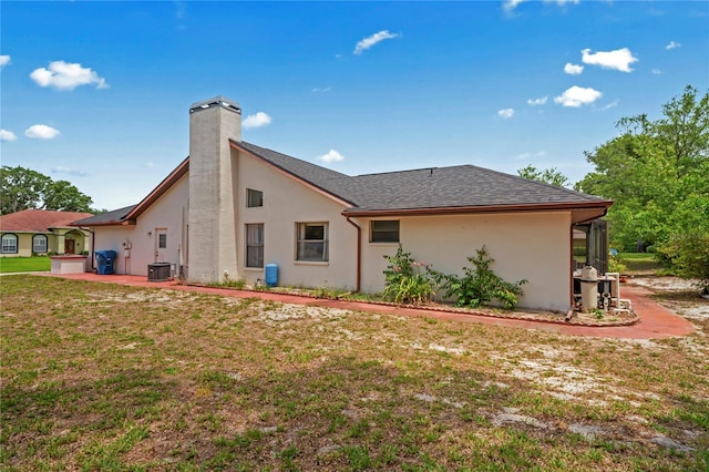 128 Oak Lake Dr, Spring Hill, FL 34608 - back of house featuring central AC unit, a chimney, a yard, and stucco siding