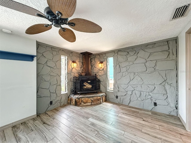 6601 Nautical Isle, Hudson, FL 34667 - unfurnished living room featuring a textured ceiling, a wood stove, light wood-style flooring, and a ceiling fan