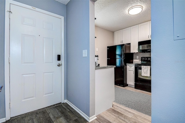 10670 43rd St N Unit 204, Clearwater, FL 33762 - kitchen with black appliances, wood finished floors, white cabinets, a textured ceiling, and baseboards