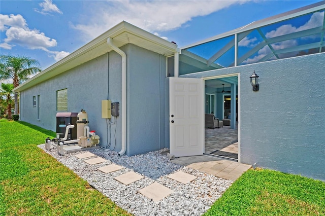 10250 Locker Dr, Spring Hill, FL 34608 - view of home's exterior featuring a lawn, glass enclosure, stucco siding, ceiling fan, and a patio area