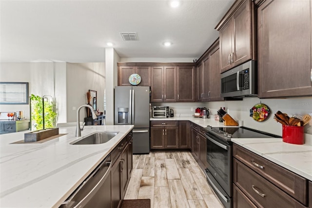11579 Weaver Hollow Rd, New Port Richey, FL 34654 - kitchen featuring stainless steel appliances, a sink, light wood-style flooring, dark brown cabinetry, and light stone countertops