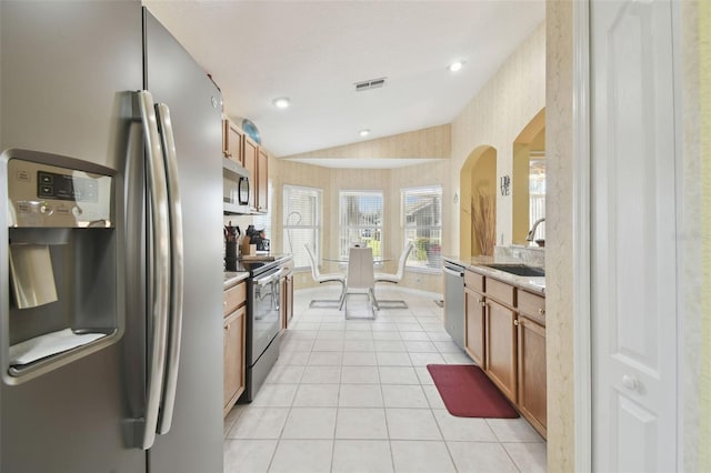 11637 Spindrift Loop, Hudson, FL 34667 - kitchen with stainless steel appliances, lofted ceiling, wallpapered walls, light tile patterned flooring, and brown cabinets