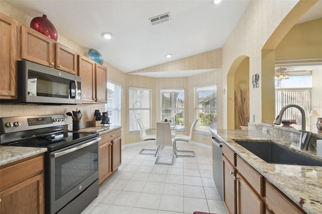 11637 Spindrift Loop, Hudson, FL 34667 - kitchen with stainless steel appliances, lofted ceiling, wallpapered walls, light tile patterned floors, and arched walkways