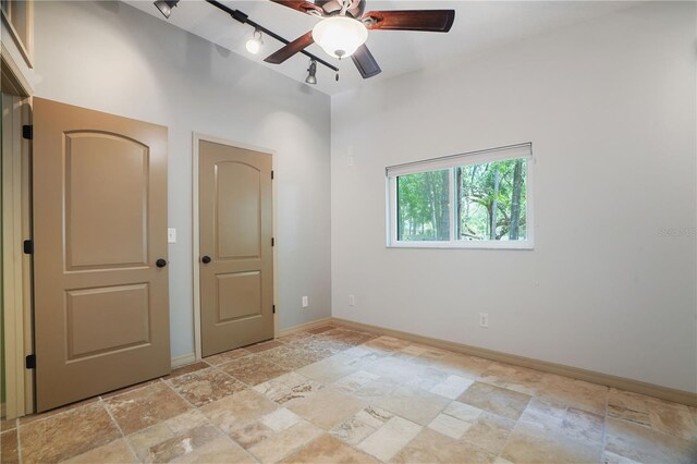 8518 Quail Hollow Blvd, Wesley Chapel, FL 33544 - unfurnished bedroom featuring stone tile floors, baseboards, a ceiling fan, and track lighting