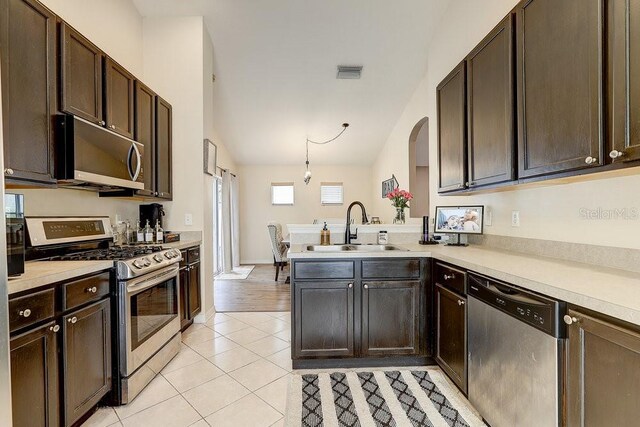 8335 Crescent Moon Dr, New Port Richey, FL 34655 - kitchen featuring stainless steel appliances, a sink, dark brown cabinets, light tile patterned floors, and high vaulted ceiling