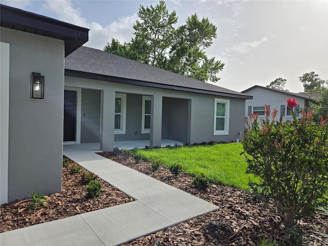 12064 Cradock St, Spring Hill, FL 34608 - property entrance with stucco siding, a lawn, covered porch, and a shingled roof