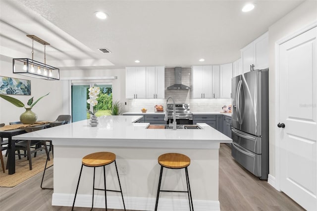 12064 Cradock St, Spring Hill, FL 34608 - kitchen featuring appliances with stainless steel finishes, wall chimney exhaust hood, a sink, a kitchen island with sink, and light wood-type flooring