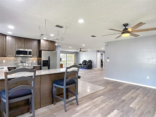 11340 Corinthian St, Spring Hill, FL 34609 - kitchen with appliances with stainless steel finishes, a ceiling fan, dark brown cabinetry, light wood-style flooring, and a textured ceiling