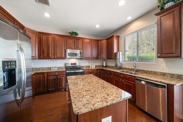 17905 Machair Ln, Land O Lakes, FL 34638 - kitchen with stainless steel appliances, a sink, dark wood-style flooring, a kitchen island, and light stone counters
