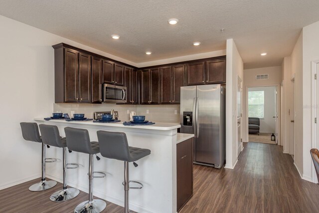 5520 White Marlin Ct, New Port Richey, FL 34652 - kitchen featuring appliances with stainless steel finishes, dark brown cabinetry, baseboards, dark wood-style flooring, and a kitchen bar