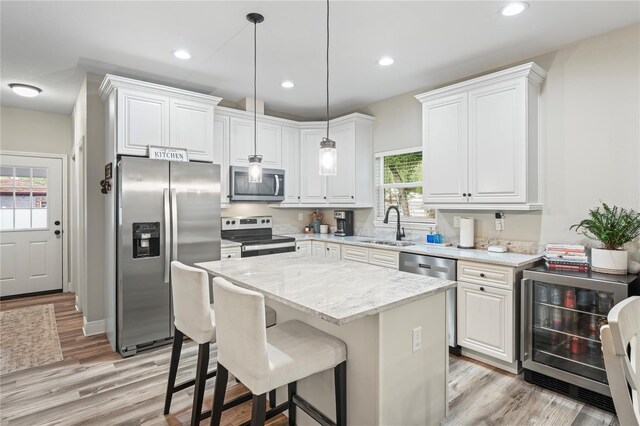 1601 E 98th Ave, Tampa, FL 33612 - kitchen with stainless steel appliances, a sink, light wood-style flooring, white cabinets, and a kitchen island