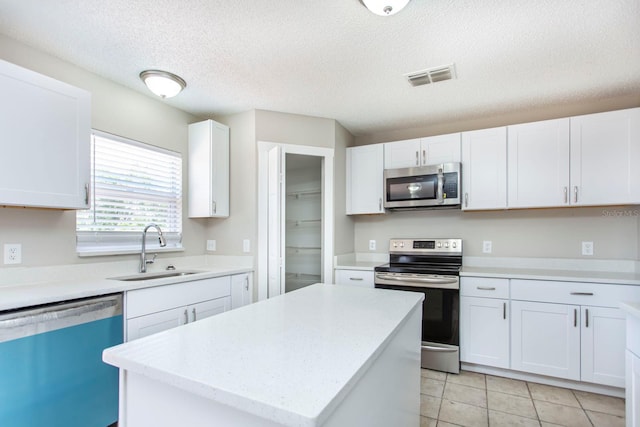 10386 Norvell Rd, Spring Hill, FL 34608 - kitchen with stainless steel appliances, white cabinetry, a textured ceiling, a kitchen island, and light tile patterned floors