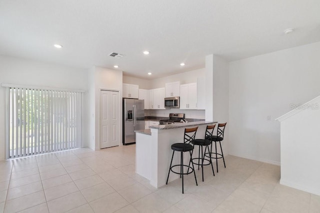 8305 Crescent Oaks Dr, New Port Richey, FL 34655 - kitchen featuring appliances with stainless steel finishes, a peninsula, a kitchen breakfast bar, white cabinetry, and dark stone countertops
