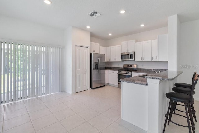 8305 Crescent Oaks Dr, New Port Richey, FL 34655 - kitchen with appliances with stainless steel finishes, a peninsula, a breakfast bar area, white cabinetry, and dark stone counters