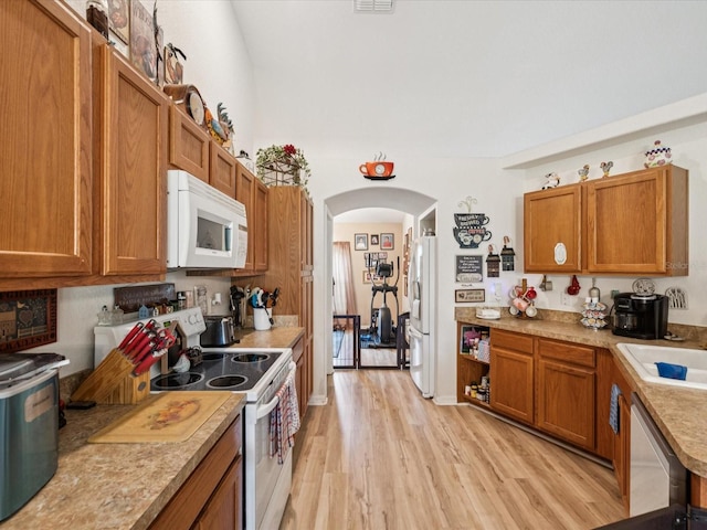 12229 Barnevelde Rd, Weeki Wachee, FL 34614 - kitchen featuring white appliances, light wood-style flooring, arched walkways, and brown cabinets