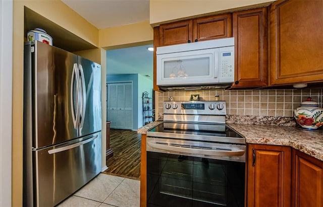 3841 Lanyard Ct Unit B, New Port Richey, FL 34652 - kitchen with appliances with stainless steel finishes, brown cabinets, backsplash, light tile patterned floors, and light stone counters