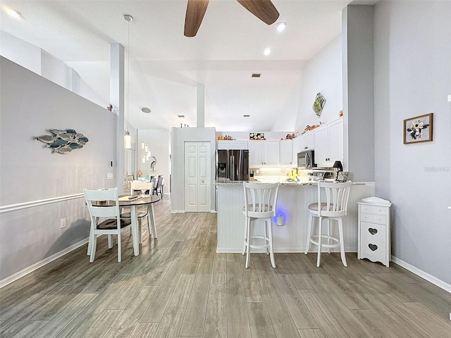 7518 Mediterranean Ct, Hudson, FL 34667 - kitchen with stainless steel fridge with ice dispenser, a peninsula, high vaulted ceiling, a ceiling fan, and light wood-type flooring