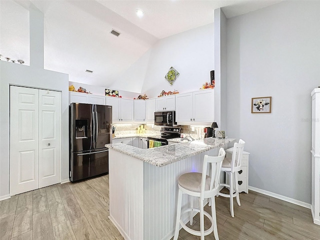 7518 Mediterranean Ct, Hudson, FL 34667 - kitchen featuring fridge with ice dispenser, stainless steel range with electric stovetop, a peninsula, light wood-style flooring, and high vaulted ceiling
