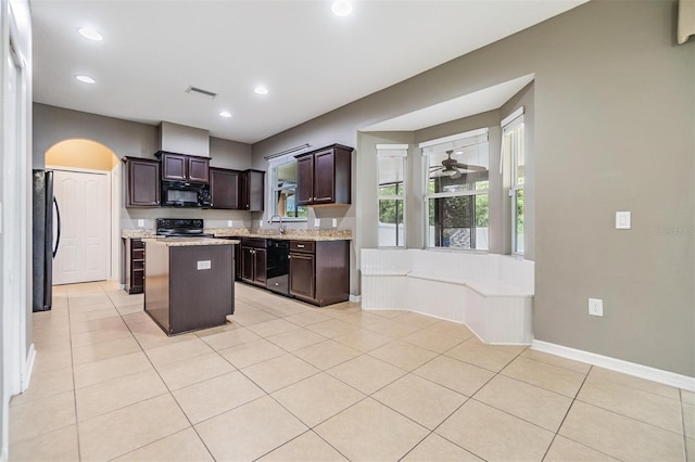 1104 Ketzal Dr, Trinity, FL 34655 - kitchen with black appliances, a center island, dark brown cabinets, light tile patterned flooring, and arched walkways