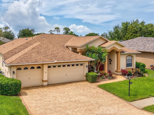 11144 Brambleleaf Way, Hudson, FL 34667 - view of front of house featuring stucco siding, decorative driveway, a garage, and roof with shingles