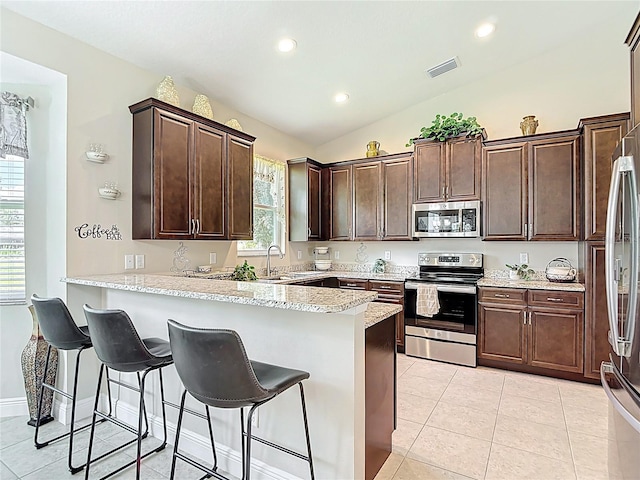 12323 House Finch, Weeki Wachee, FL 34614 - kitchen with appliances with stainless steel finishes, vaulted ceiling, a peninsula, dark brown cabinetry, and a breakfast bar area