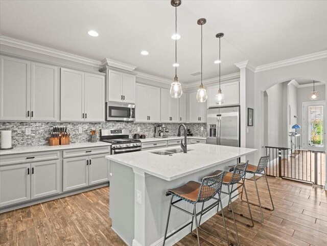 6130 Colmar Pl, Apollo Beach, FL 33572 - kitchen featuring stainless steel appliances, arched walkways, wood finished floors, a kitchen breakfast bar, and decorative backsplash