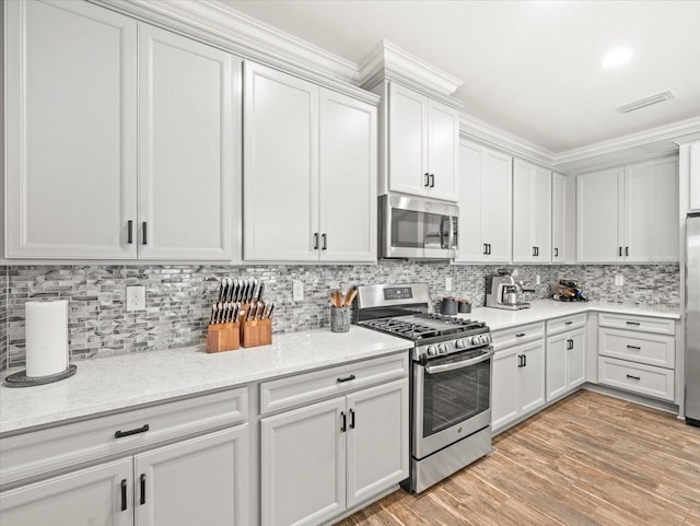 6130 Colmar Pl, Apollo Beach, FL 33572 - kitchen featuring appliances with stainless steel finishes, decorative backsplash, light wood-type flooring, white cabinets, and crown molding