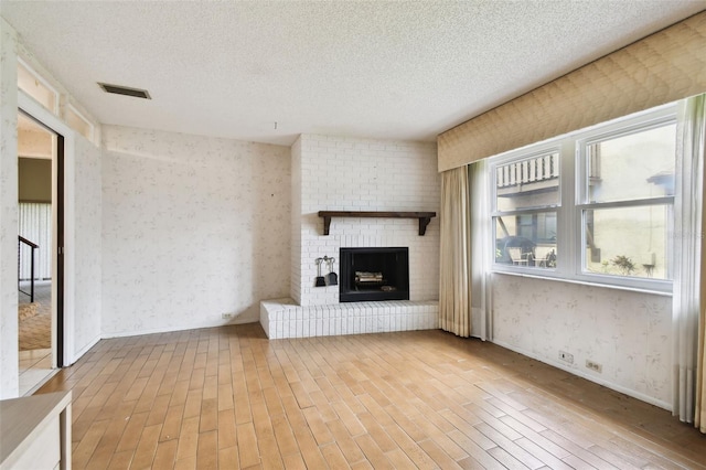 2101 Sunset Point Rd Unit 201, Clearwater, FL 33765 - unfurnished living room with a textured ceiling, wood finished floors, wallpapered walls, and a brick fireplace