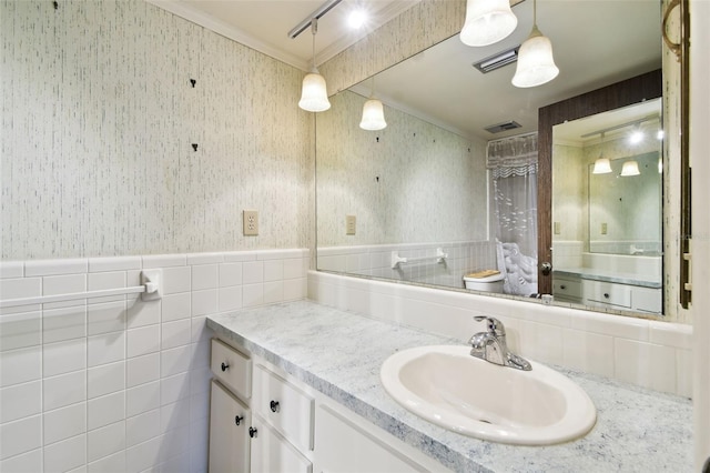 2101 Sunset Point Rd Unit 201, Clearwater, FL 33765 - bathroom featuring wallpapered walls, ornamental molding, vanity, a wainscoted wall, and tile walls