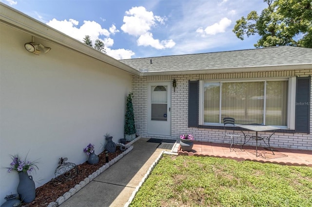 7701 Anaheim Ave, New Port Richey, FL 34655 - property entrance featuring brick siding, roof with shingles, a yard, and a patio
