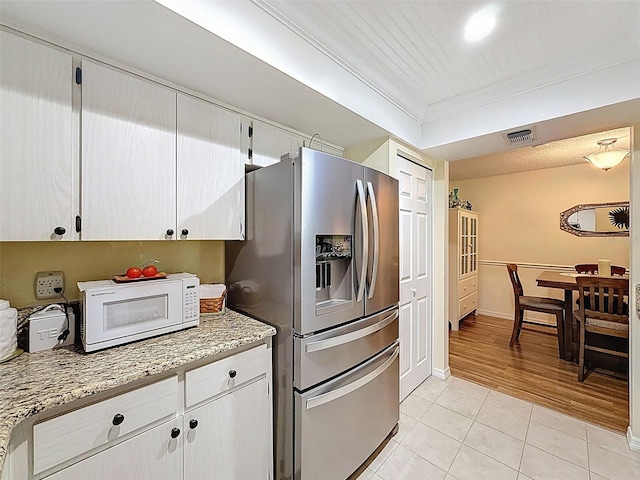 8130 Bugle Ct Unit 3, Port Richey, FL 34668 - kitchen with stainless steel fridge, white microwave, light tile patterned floors, light stone counters, and white cabinets