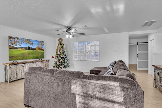 15950 Adobe Dr, Hudson, FL 34667 - living room featuring light wood-type flooring, a barn door, ceiling fan, and a textured ceiling