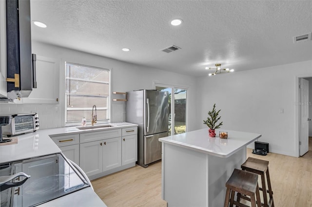 15950 Adobe Dr, Hudson, FL 34667 - kitchen with freestanding refrigerator, light wood-style flooring, light countertops, a textured ceiling, and a breakfast bar area