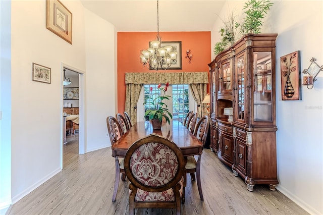 dining space with a chandelier, light wood-style flooring, and a towering ceiling