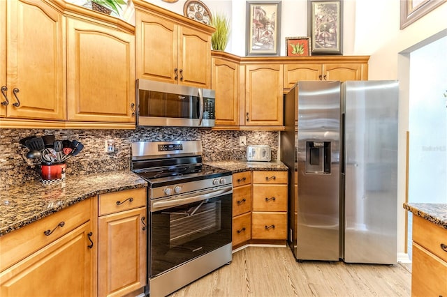 kitchen with stainless steel appliances, light wood-type flooring, dark stone counters, and tasteful backsplash