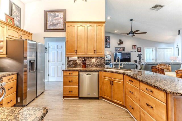 kitchen featuring appliances with stainless steel finishes, a peninsula, lofted ceiling, a ceiling fan, and dark stone countertops