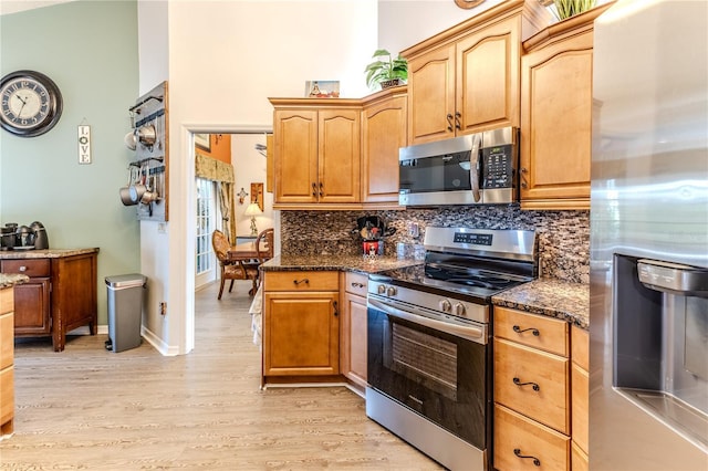 kitchen featuring stainless steel appliances, decorative backsplash, dark stone counters, and light wood-style floors